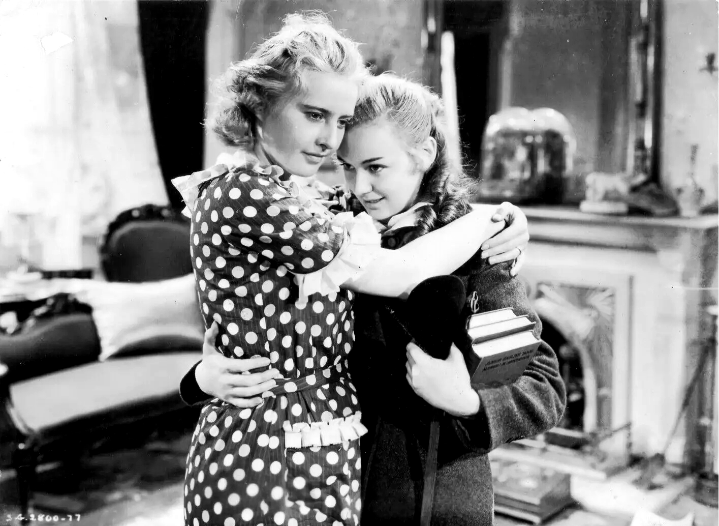 Barbara Stanwyck in a polka-dot dress embracing Anne Shirley, who holds a stack of books, in Stella Dallas.