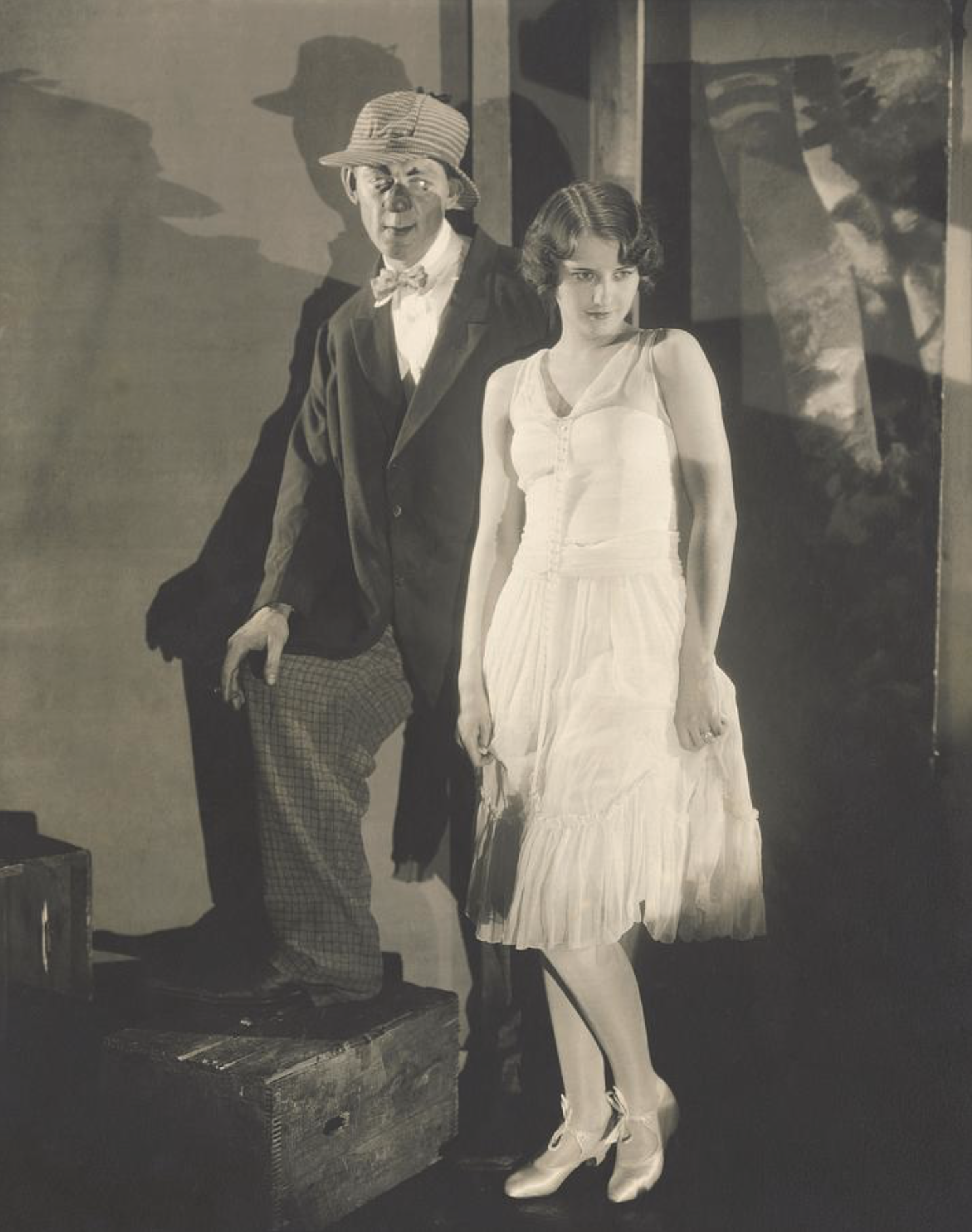 Hal Skelly in a bow tie and hat standing beside Barbara Stanwyck in a white dress for the Broadway play Burlesque.