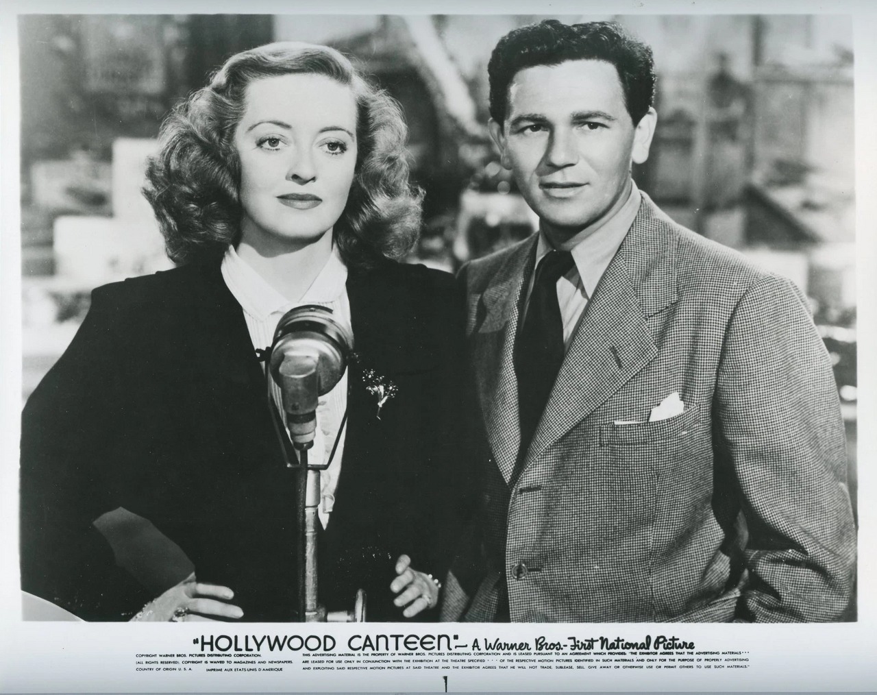 Bette Davis and John Garfield stand together at a microphone in a Hollywood Canteen publicity photograph.