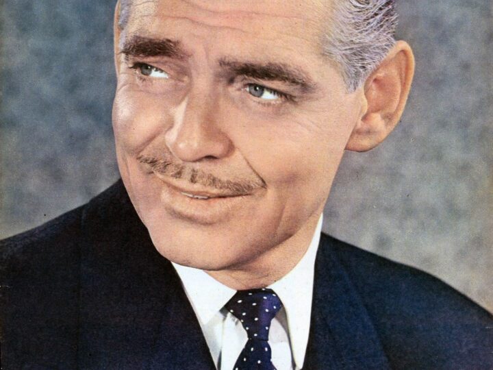 Colour 1949 portrait of Clark Gable in a dark suit and spotted tie, looking to his right.