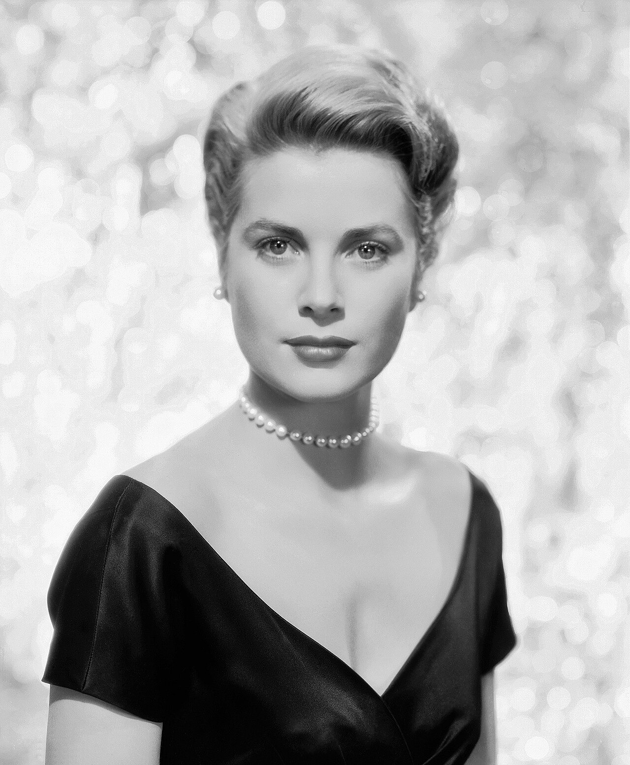 Black-and-white studio portrait of Grace Kelly in a dark evening dress and pearl necklace.