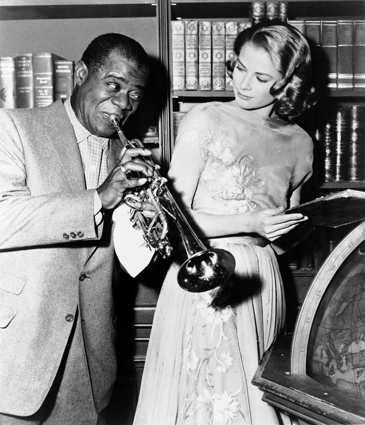 Louis Armstrong smiles with his trumpet while Grace Kelly looks on during production of High Society.