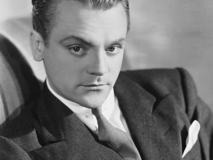 James Cagney seated in a dark suit and tie, looking to the left of the camera in a 1930s studio portrait.