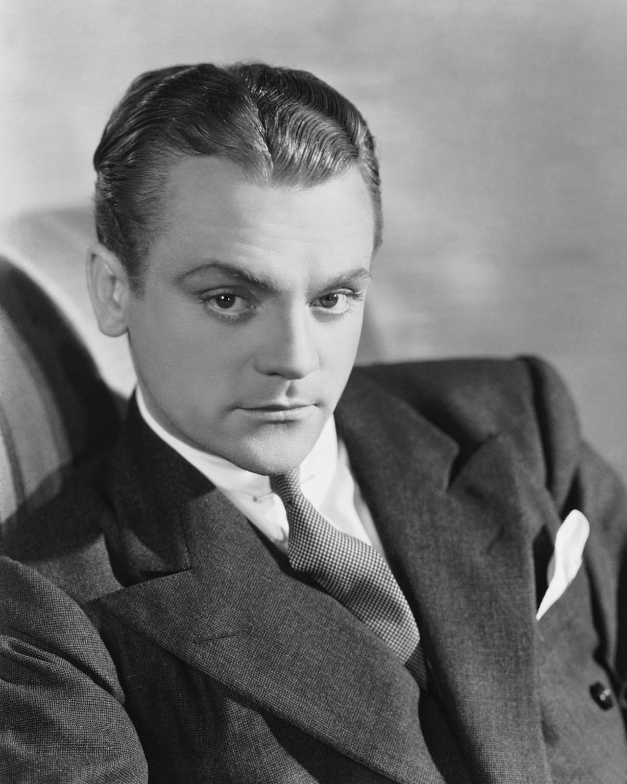 James Cagney seated in a dark suit and tie, looking to the left of the camera in a 1930s studio portrait.