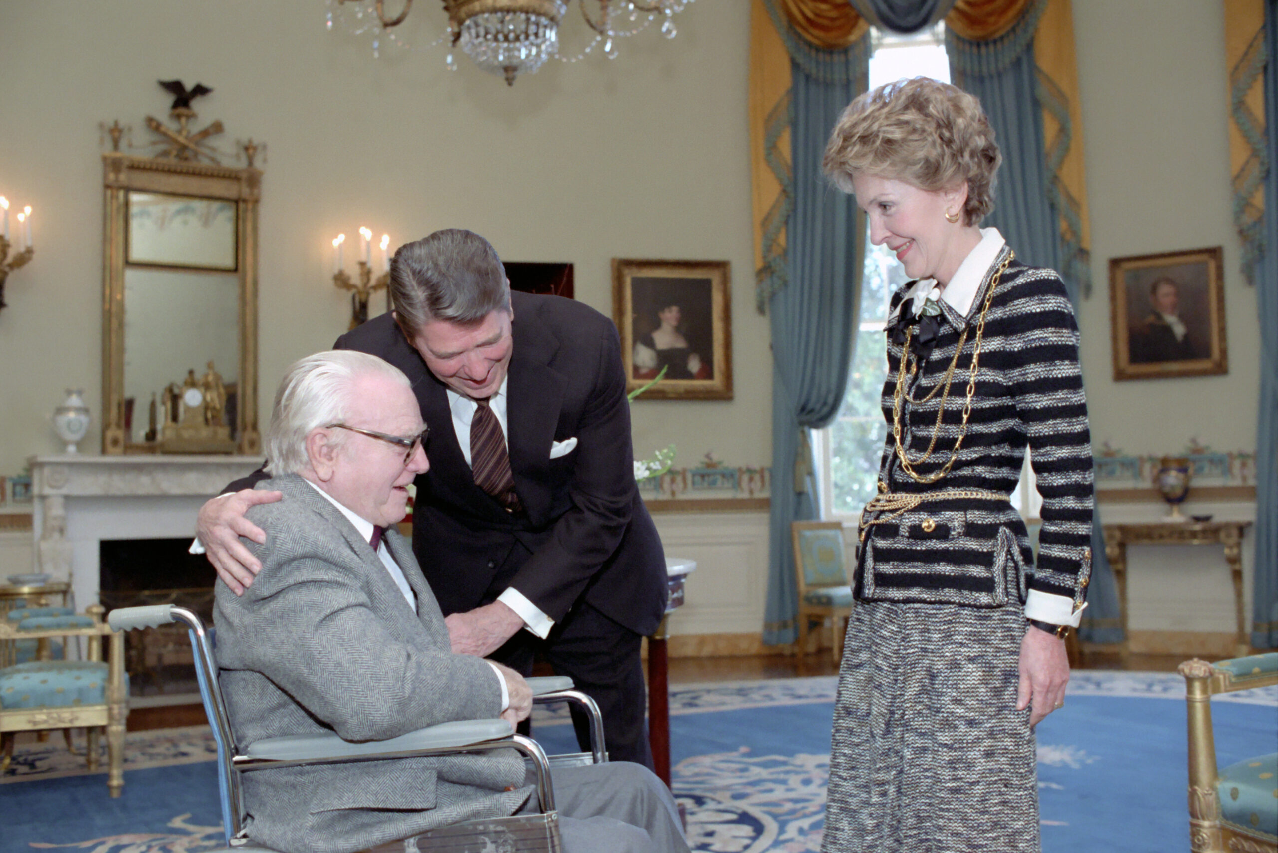 James Cagney sits in a wheelchair as President Ronald Reagan leans towards him and Nancy Reagan stands nearby in 1984.