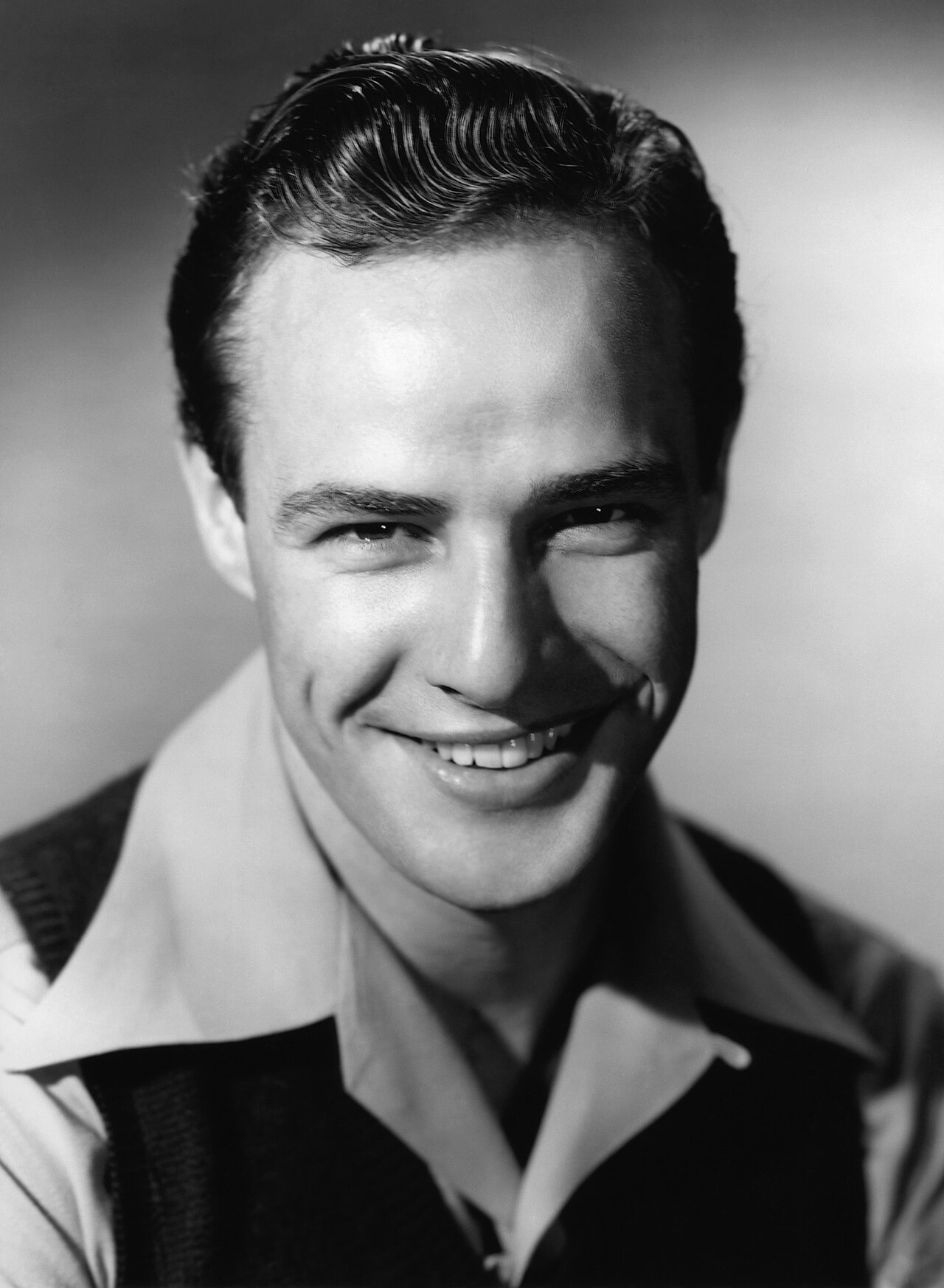 Black-and-white early-career studio portrait of a smiling Marlon Brando for The Men.
