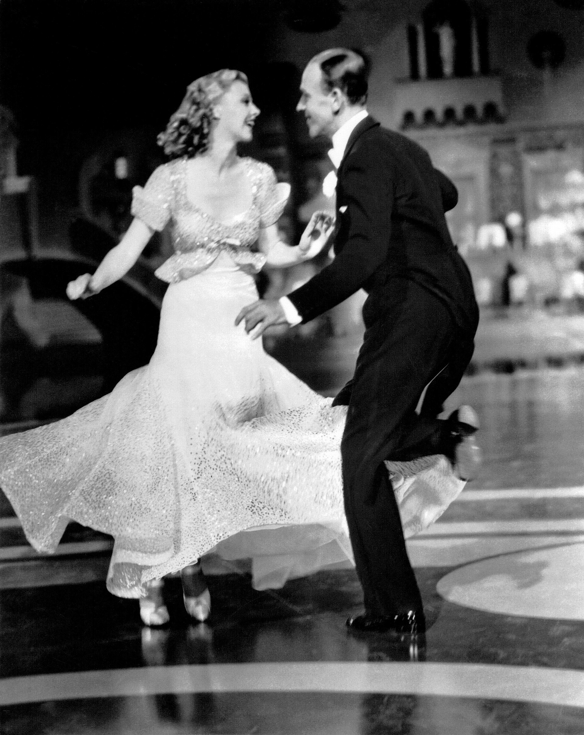 Fred Astaire in top hat and tails dancing with Ginger Rogers in a white gown in Top Hat.