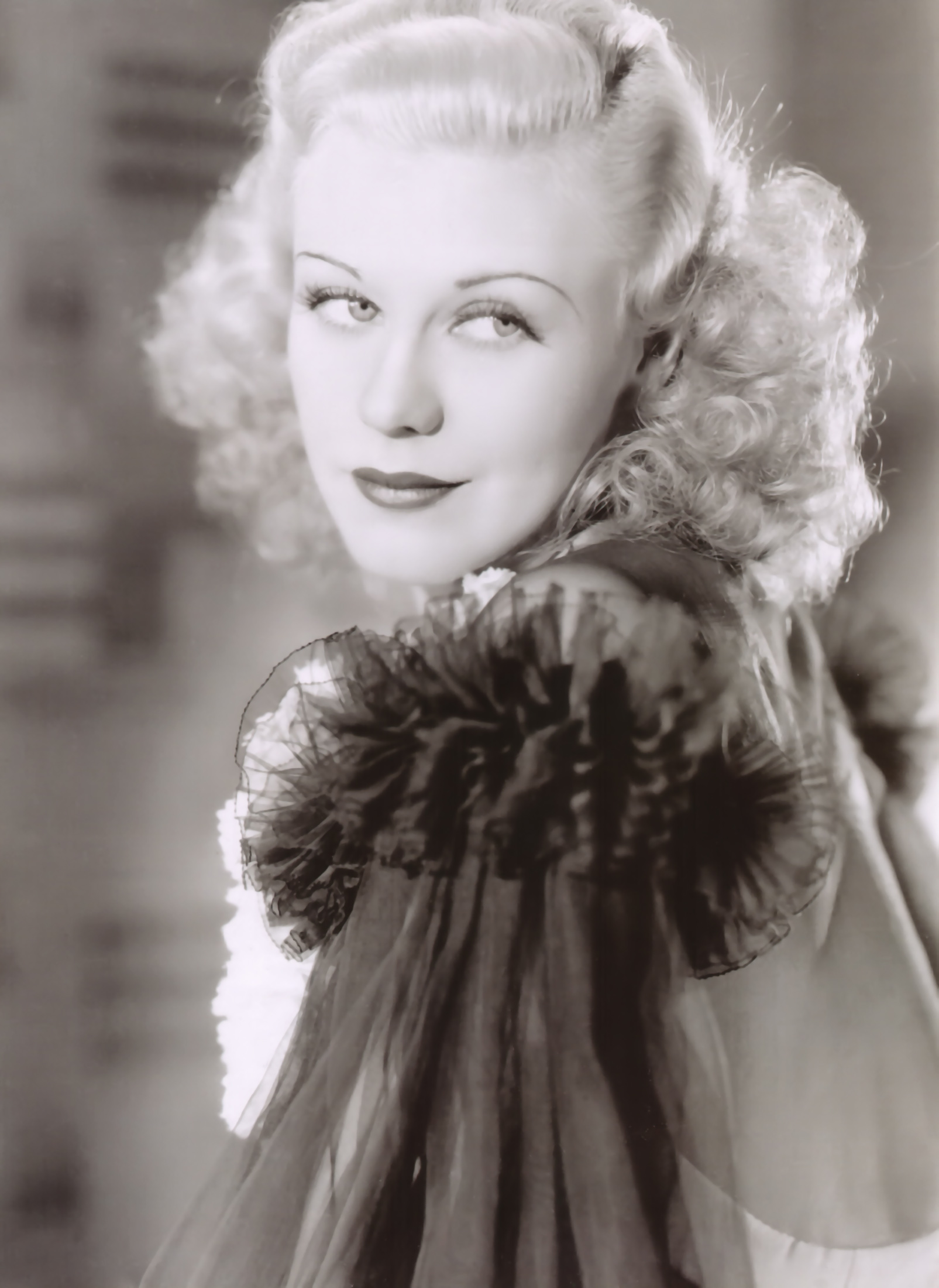 Ginger Rogers looks towards the camera in a softly lit black-and-white studio portrait from the 1930s.