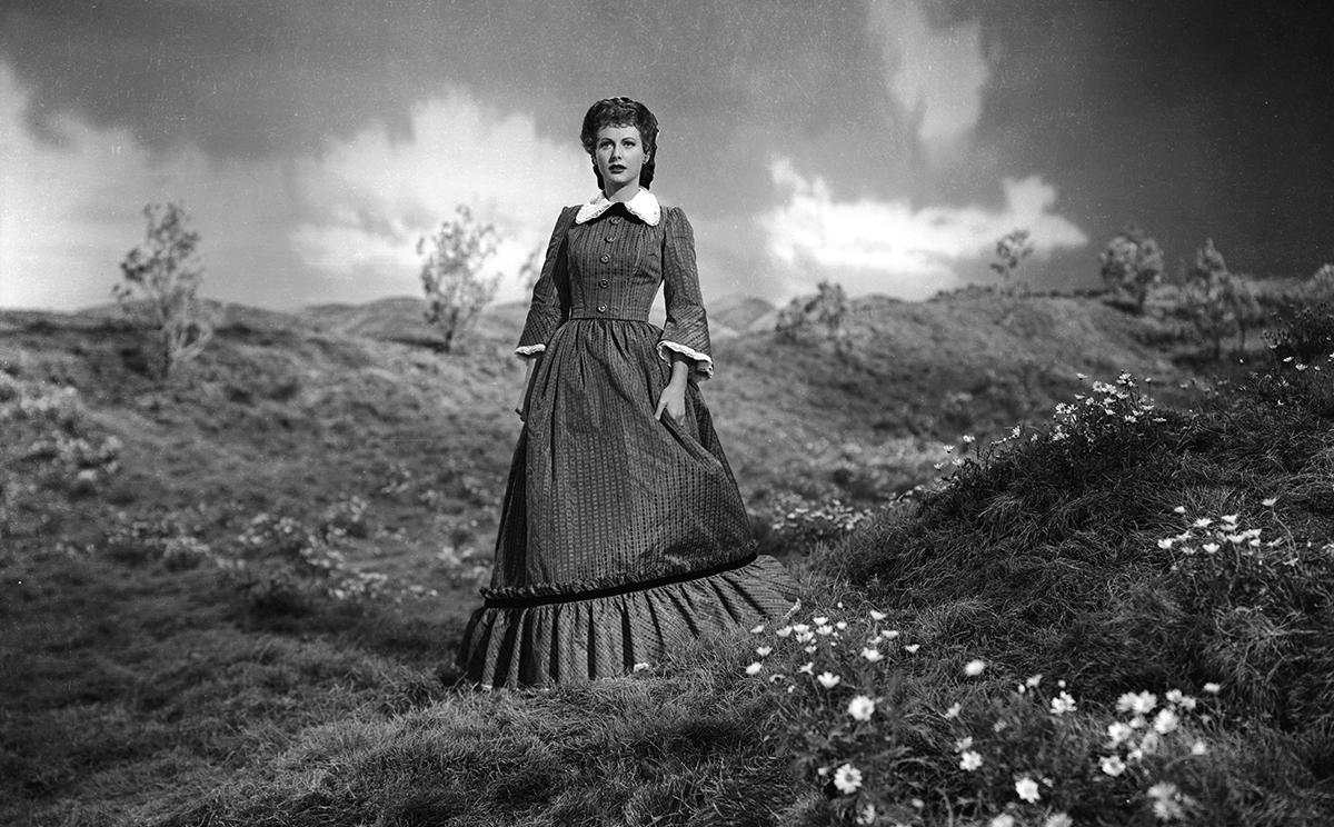 Hedy Lamarr in a dark period dress standing on a windswept landscape in Experiment Perilous.