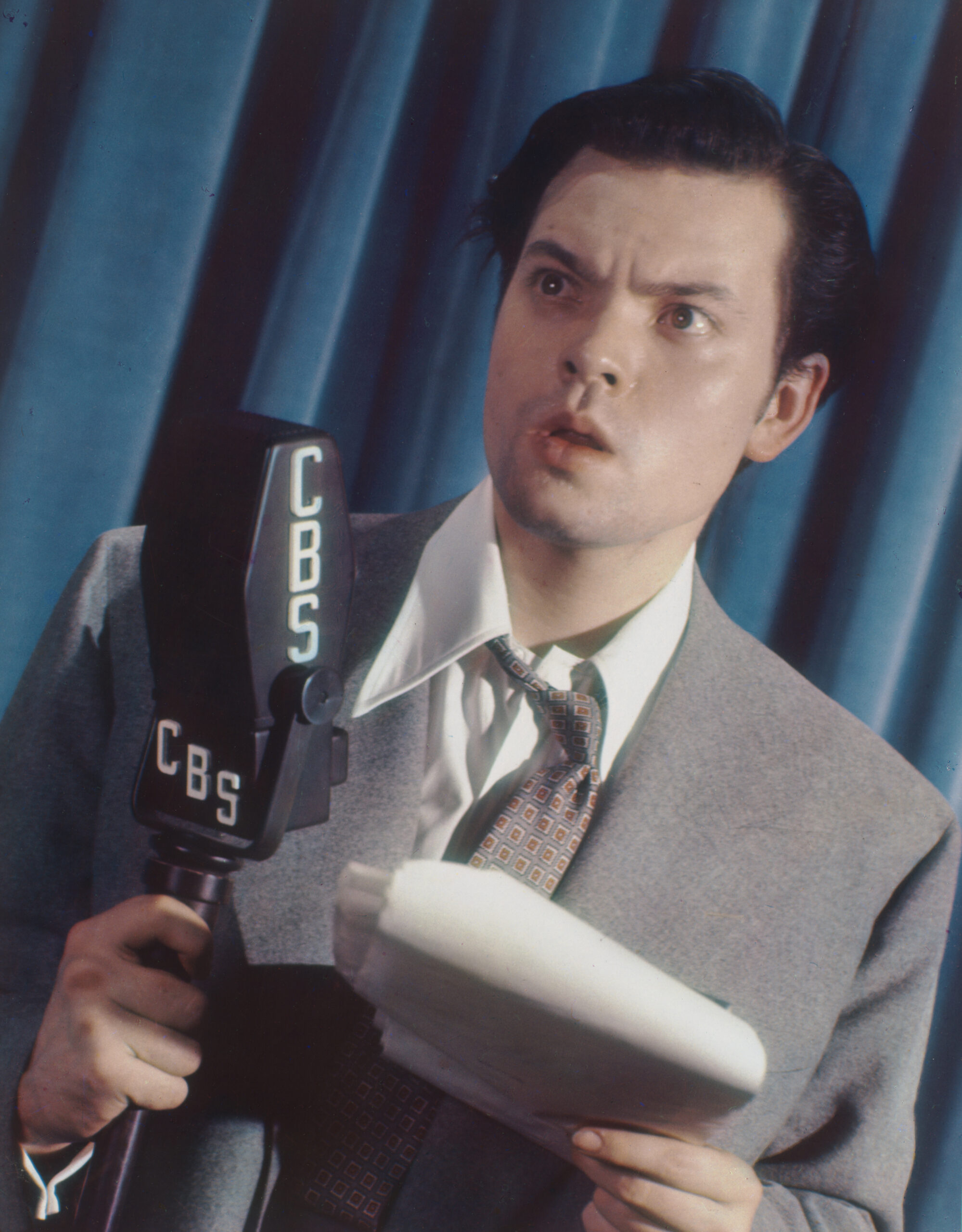 Colour portrait of Orson Welles holding a CBS microphone and a script in 1939.
